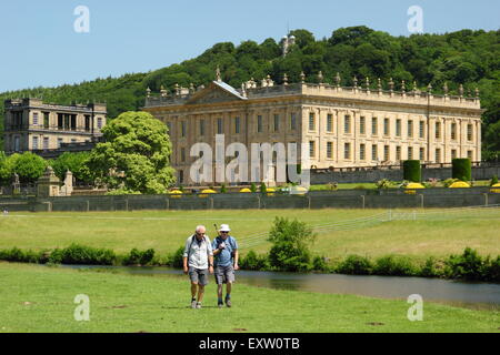 Two men walk on the banks of the River Derwent by Chatsworth House in the Peak District on a glorious summer day, Derbyshire UK