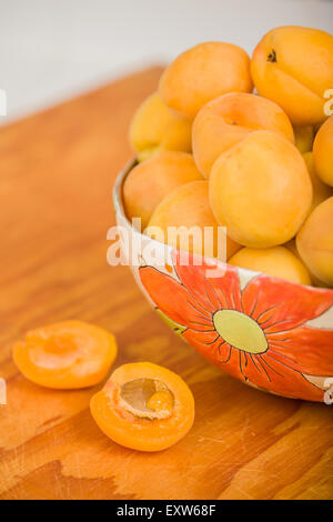 Bowl of apricots in handmade pottery bowl resting on a wooden cutting board Stock Photo