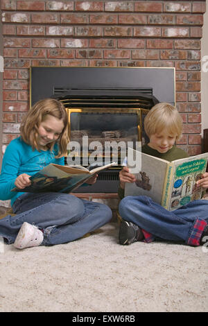 Boy and girl enjoying reading in front of a gas fireplace in a family room.  Concepts: informal education, learning, fascination Stock Photo