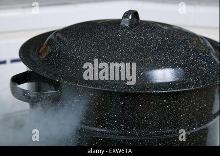 Large blue pot sitting on the stove just starting to boil, but the lid is still firmly on Stock Photo