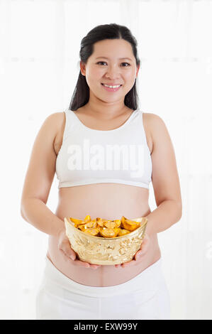 Pregnant woman holding gold ingot and smiling at the camera, Stock Photo
