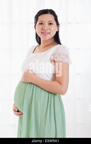 Pregnant woman smiling at the camera with hands on abdomen, Stock Photo