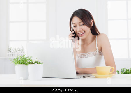 Young woman holding mobile phone and using laptop,