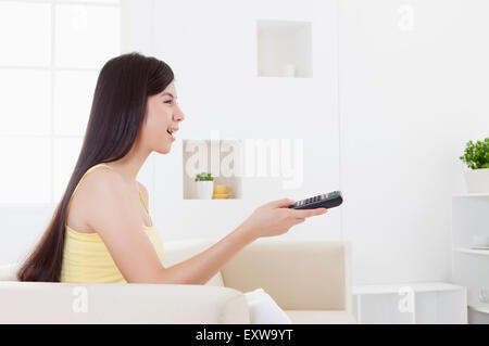 Young woman holding remote control and looking away with smile, Stock Photo