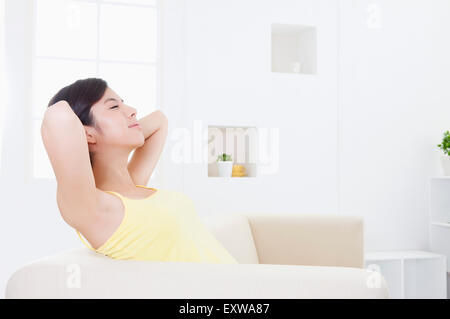 Young woman sitting on sofa with hands behind head, Stock Photo