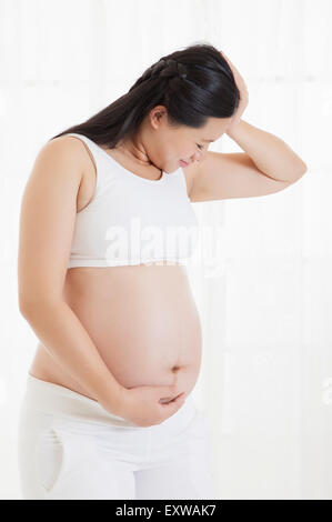 Pregnant woman looking down with hand on abdomen, Stock Photo
