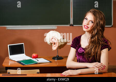 Excellent pupil sitting at a desk. On the table is a layout of the human ear, laptop, notebook and apple. Stock Photo