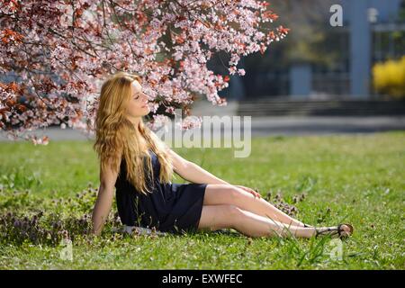 Young woman sitting on meadow in park Stock Photo