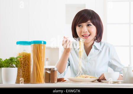 Young woman eating spaghetti and looking away with smile, Stock Photo