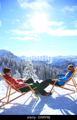 Two women in lounger in snow, Tegelberg, Ammergau Alps, Allgaeu, Bavaria, Germany, Europe Stock Photo