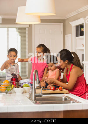 Mother and children (2-3, 6-7, 8-9) preparing fruit cocktails Stock Photo