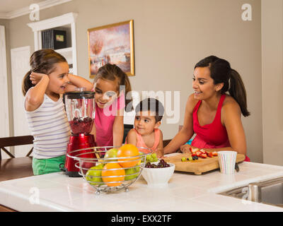 Mother and children (2-3, 6-7, 8-9) preparing fruit cocktails Stock Photo