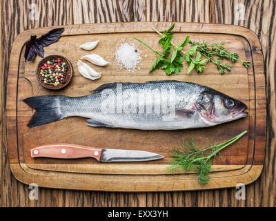 Fish - sea bass on a wooden board with spices and herbs. Stock Photo