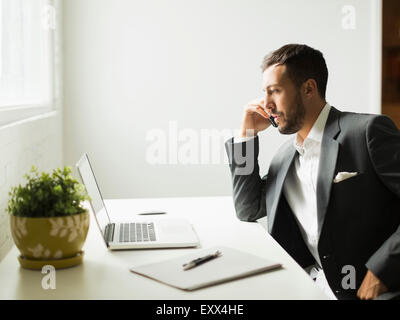 Young man sitting at desk and looking at laptop Stock Photo