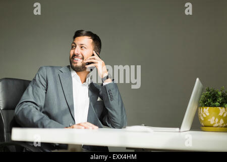 Young man sitting at desk and talking on phone Stock Photo