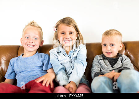 Smiling children (2-3, 4-5) sitting on sofa Stock Photo