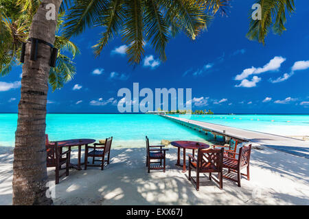 Tables and chairs in the shadow of palm tree on amazing tropical island Stock Photo