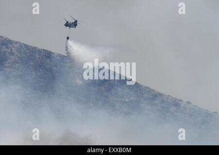 Athens, Greece. 17th July 2015. A helicopter deploys water on the wildfire at the Hymettus mountain range. Wildfires have broken out in the Hymettos mountain range, on the southern outskirts of Athens. Firefighting efforts are hampered by the current Greek crisis, which left many fire fighting equipment in an unusable condition, and strong winds in the area. Credit:  Michael Debets/Alamy Live News Stock Photo