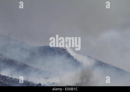 Athens, Greece. 17th July 2015. A helicopter deploys water on the wildfire at the Hymettus mountain range. Wildfires have broken out in the Hymettos mountain range, on the southern outskirts of Athens. Firefighting efforts are hampered by the current Greek crisis, which left many fire fighting equipment in an unusable condition, and strong winds in the area. Credit:  Michael Debets/Alamy Live News Stock Photo