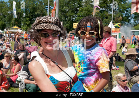 A trendy mother holding her young child dressed in colourful festival clothes in the crowds at the WOMAD world music festival Stock Photo