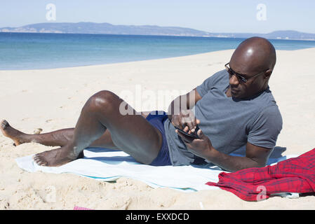 Man lying on beach, using smartphone Stock Photo