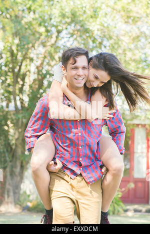 Couple together outdoors, man giving woman a piggyback ride Stock Photo