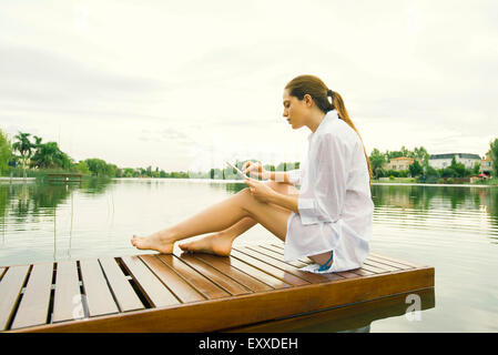 Woman relaxing on lake dock using digital tablet Stock Photo