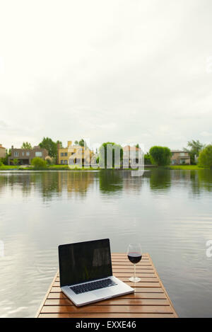 Laptop computer and wine glass on lake pier Stock Photo