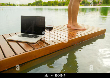 Man standing beside laptop computer and glass of wine on pier Stock Photo