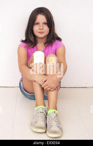 Girl hugging bandaged knees, portrait Stock Photo