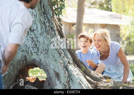 Young boy and mother hiding behind tree, playing hide-and-seek Stock Photo