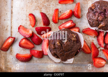 Chocolate muffins with nuts and cherry, metal background, strawberries on side, selective focus Stock Photo