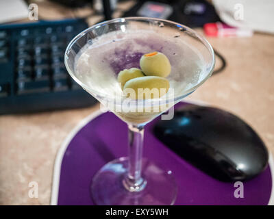 Gin martini sitting next to computer mouse with soft focus computer keyboard in background. Stock Photo