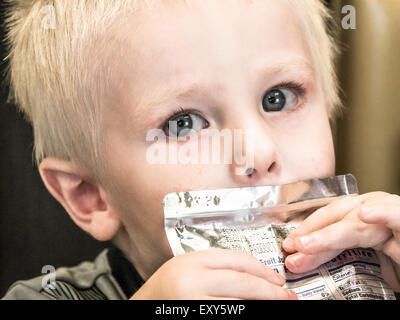 Two-year-old boy drinks juice from packet while staring directly at the camera. Stock Photo