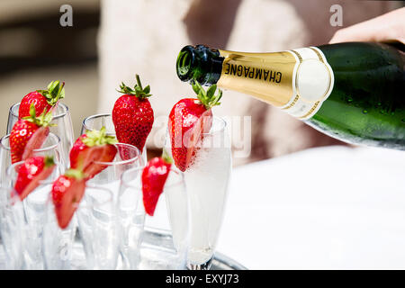 Champagne being poured into glasses decorated with strawberry's. Typical of an English garden party or wedding reception. Left on a table for guests Stock Photo