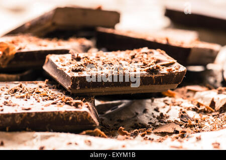 Pieces of chocolate bar with shavings on paper close up Stock Photo