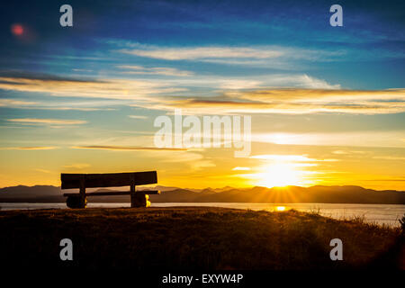 A bench overlooking a sunset on a hill overlooking Lake Champlain. Stock Photo