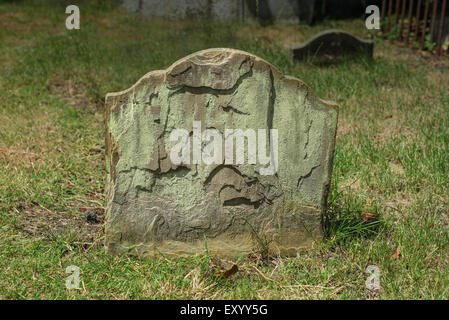Half buried ancient weathered and flaking gravestone Stock Photo