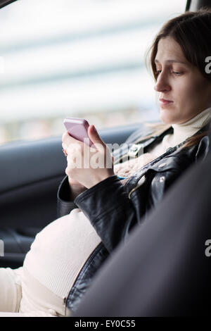 Pregnant woman texting on cell in the car Stock Photo