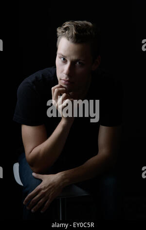 A blond, Caucasian man, sitting and leaning forward. He appears to be calm and thinking, pondering about something. Stock Photo