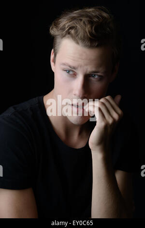 A nervous, worried man biting his nails. A dark emotional portrait. Stock Photo