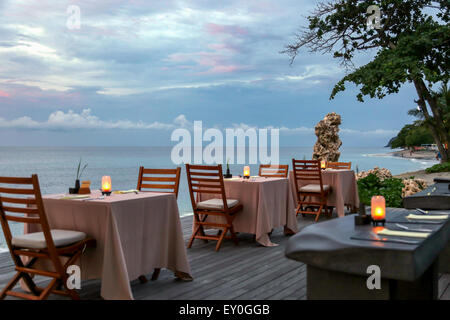 four restaurant tables on the wooden floor next to the beach during sunset time. each table has two chairs and a lamp on it. sea Stock Photo