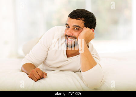 happy young Indian man lying on bed at home Stock Photo