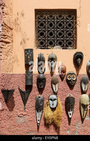 African wooden painted masks hanging on a wall beneath an Arabesque detail window in Marrakesh, Morocco Stock Photo