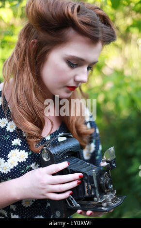 Beautiful young woman with hair in victory rolls  from 1940's holding a camera Stock Photo