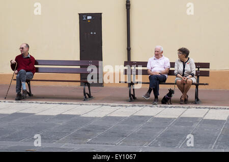 Three people sitting on street benches. Stock Photo