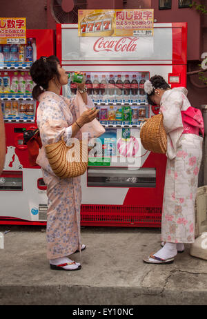 KYOTO, JAPAN - JUNE 29, 2015: two female tourists in japanese traditional yukata buy drinks from a vending machine Stock Photo
