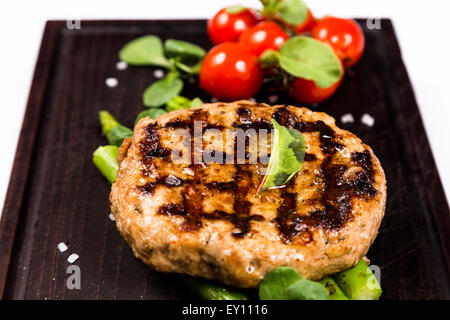 grilled meat cutlet serving with asparagus and cherry tomatoes on wooden board Stock Photo