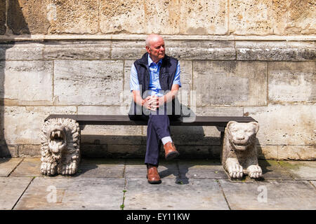Senior man sitting on bench with stone lions outside Braunschweiger Dom, Brunswick cathedral, St.Blasius Cathedral in Germany Stock Photo