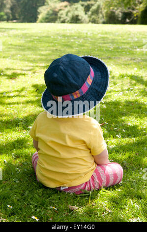 Rear view of a little girl sitting on the grass wearing a sun hat Stock Photo